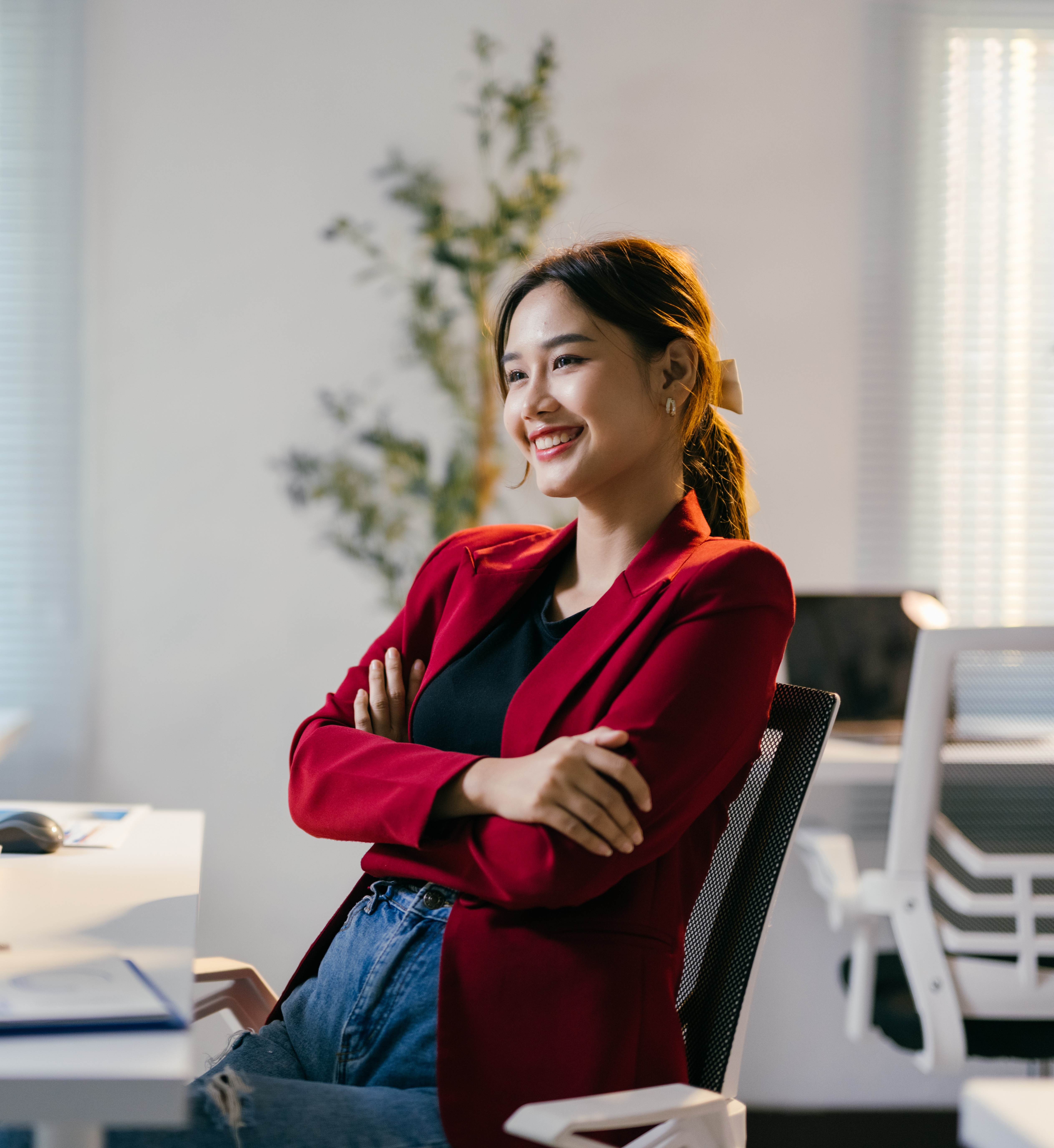Young businesswoman is sitting at her desk in a modern office, smiling with her arms crossed. She is looking away from the camera, appearing confident and successful Young businesswoman is sitting at her desk in a modern office, smiling with her arms crossed. She is looking away from the camera, appearing confident and successful