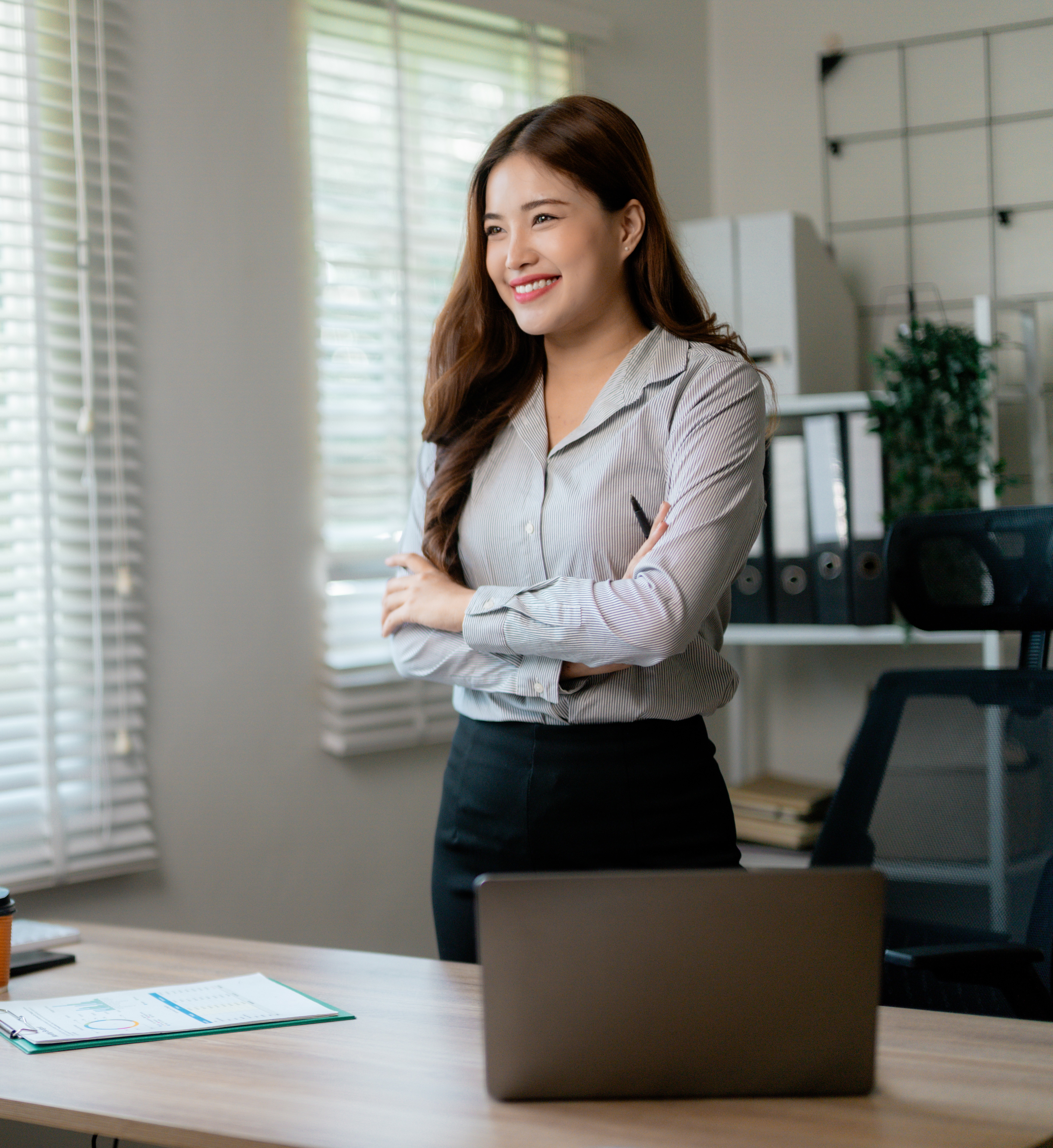 Professional Asian businesswoman smiling confidently, crossing arms near sleek workspace Professional Asian businesswoman smiling confidently, crossing arms near sleek workspace