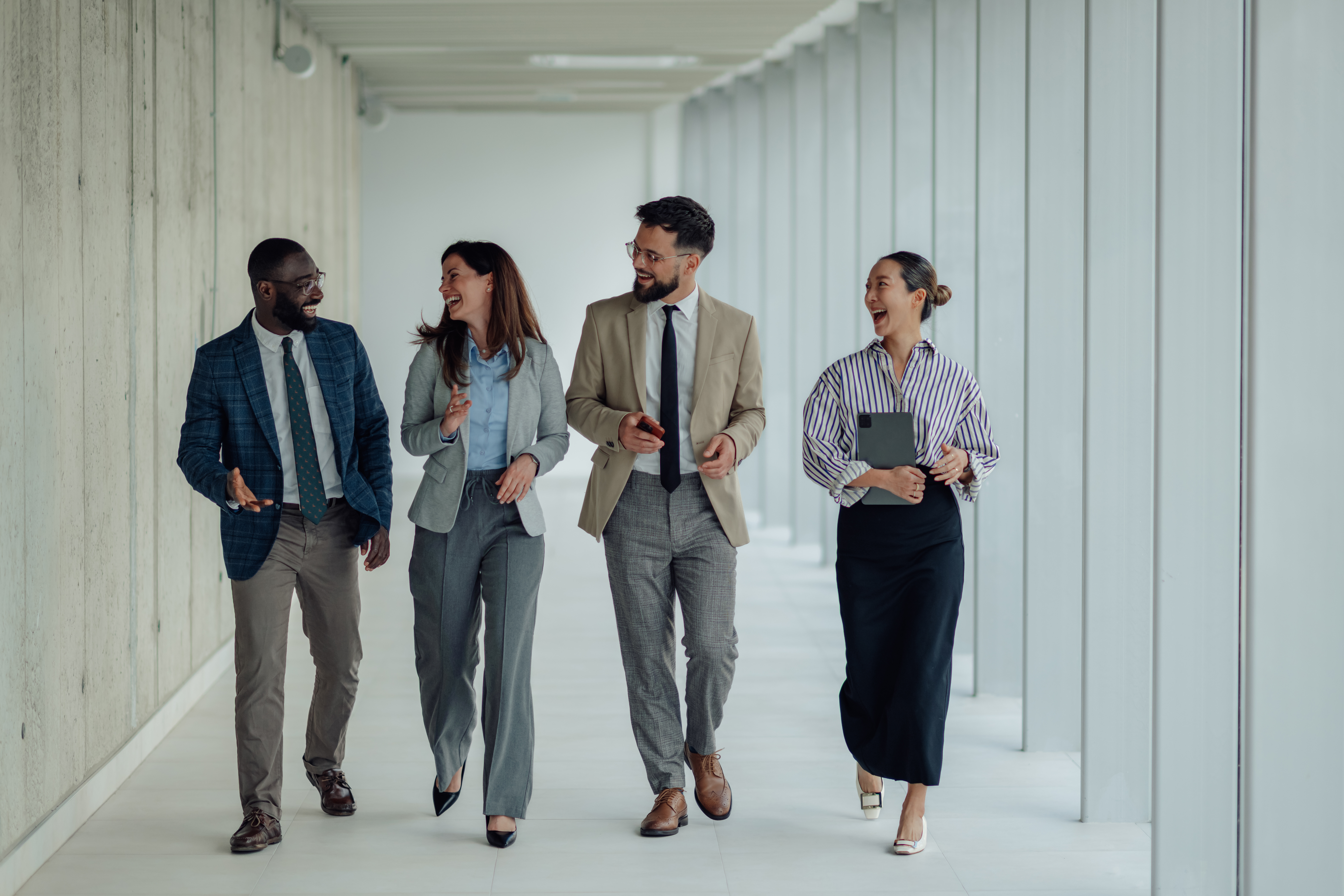 Happy multiethnic businesspeople walking and talking in office hallway